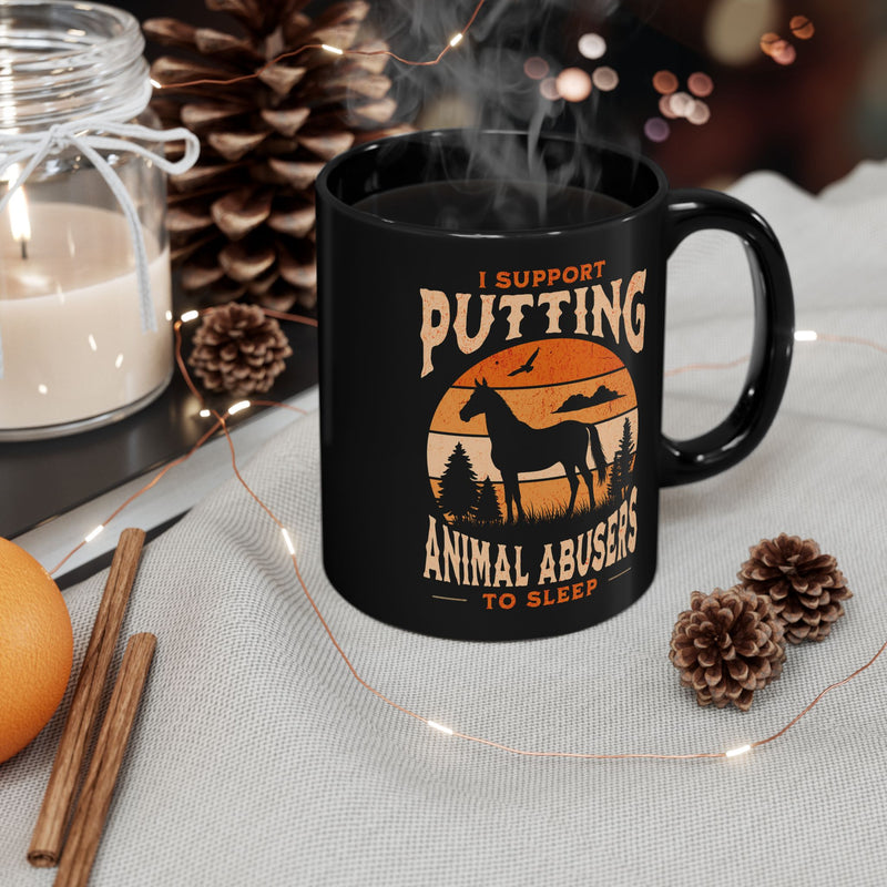 Black 11oz coffee mug (right view) with strong anti-animal abuse message, displayed in cozy holiday setting with candles, pinecones, and cinnamon sticks.