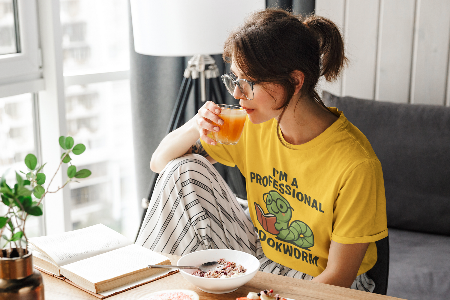 Woman in yellow shirt with a dinosaur graphic sitting on a couch, drinking juice and eating.