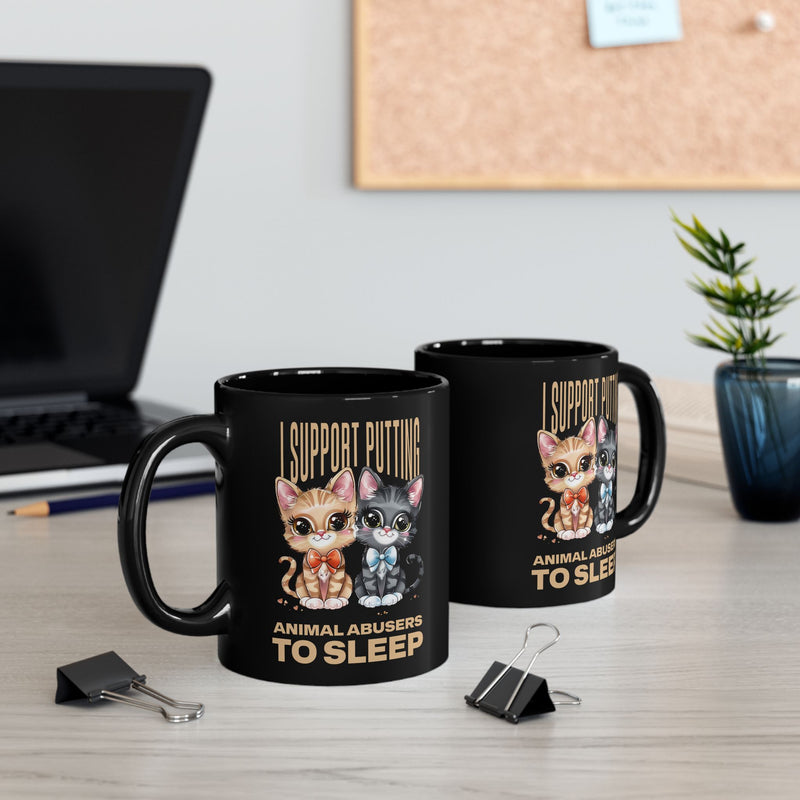 Black 11oz mugs with "I Support Putting Animal Abusers to Sleep" slogan and two cartoon kittens, on a modern office desk.